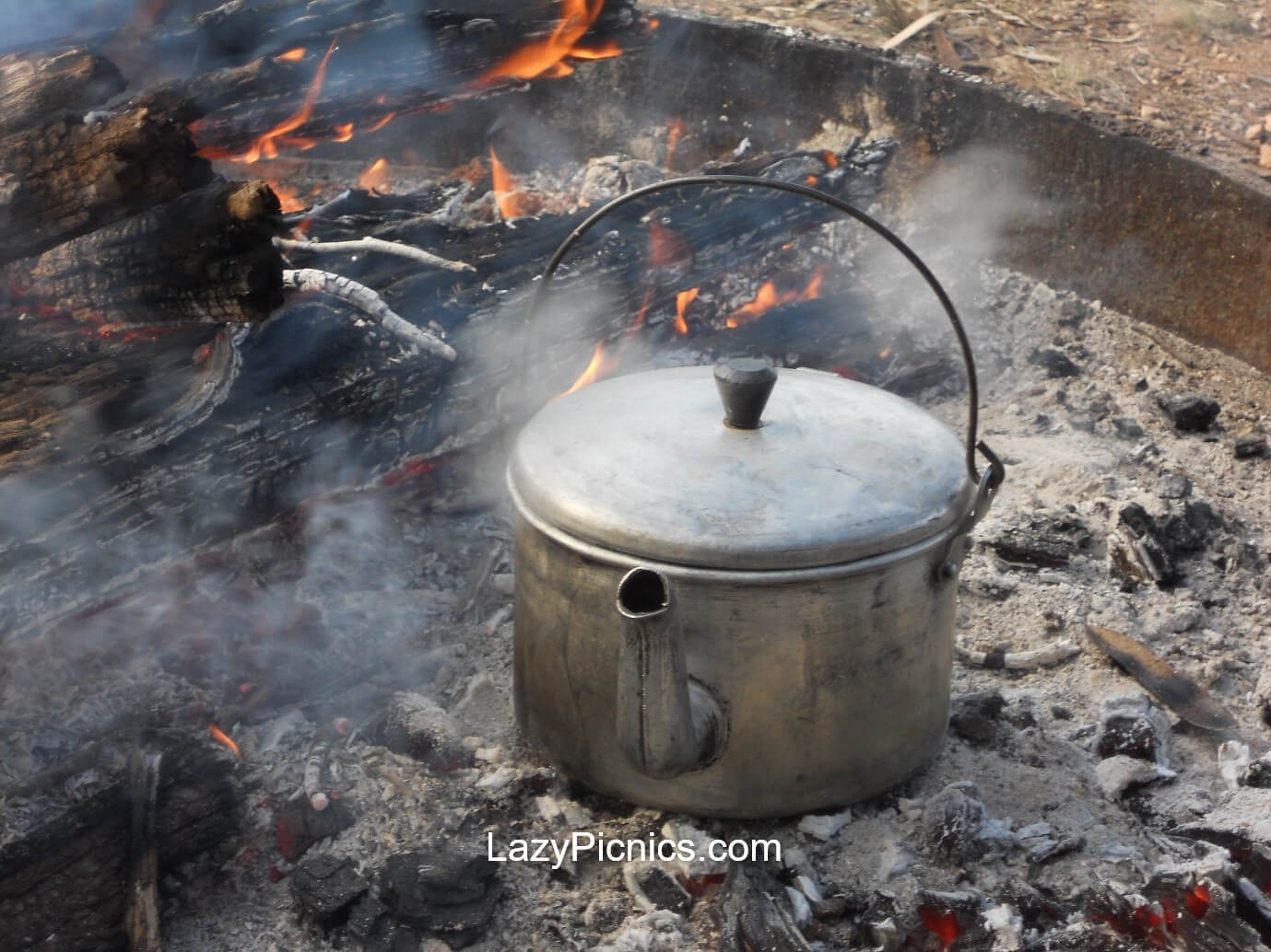 A metal bucket with lid and spout sitting on hot coals... boiling the billy on an open fire. A metal bucket with lid... boiling the billy