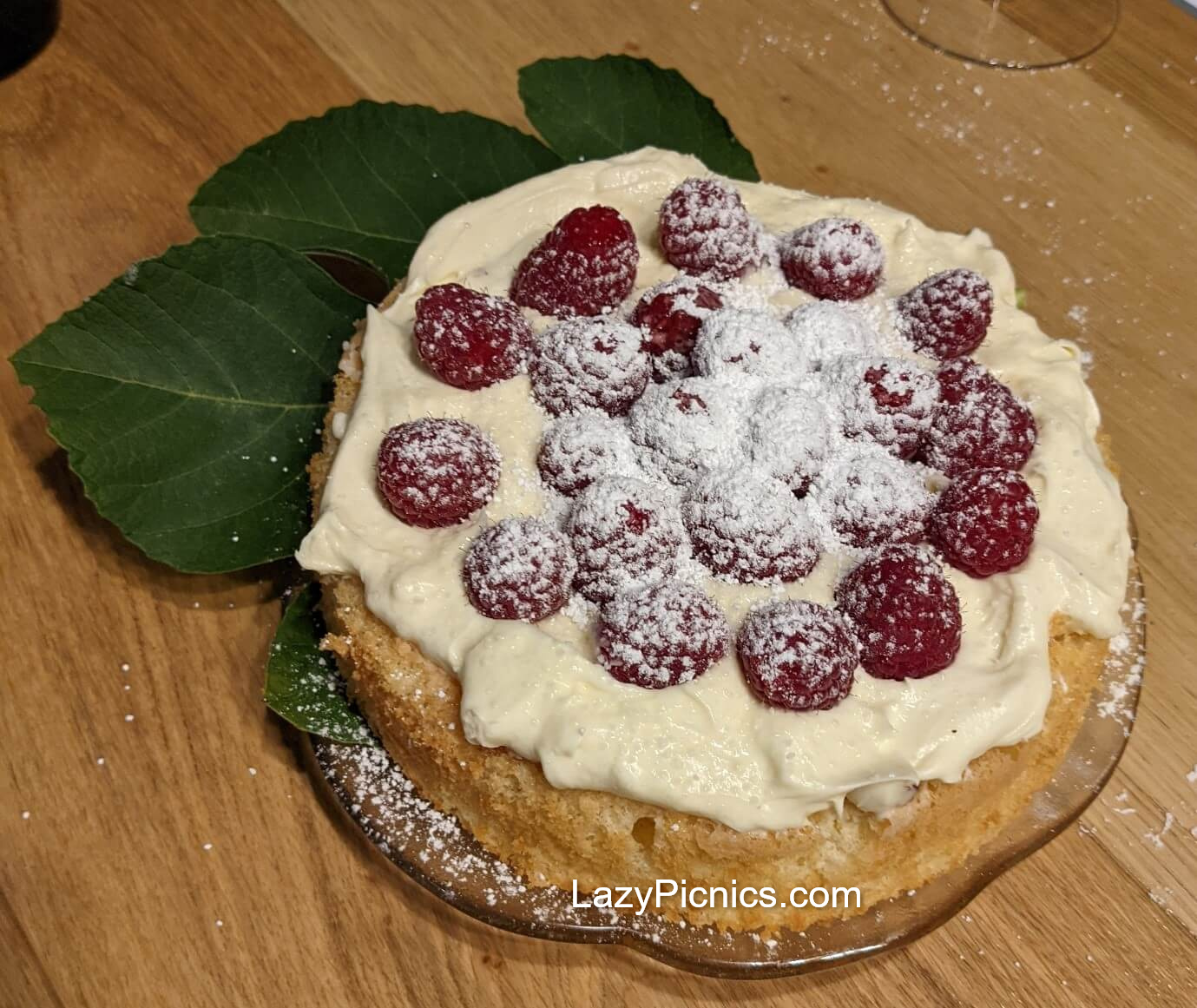 A delicious sponge cake sitting on a huge fig leaf with fig jam, cream and raspberries on top A delicious sponge cake with cream and raspberries on top